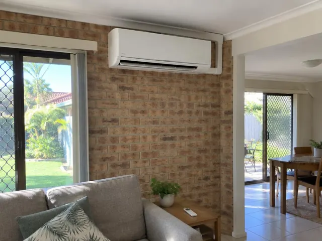 Wall-mounted split system above a brick feature wall in a tiled living room in Carrara