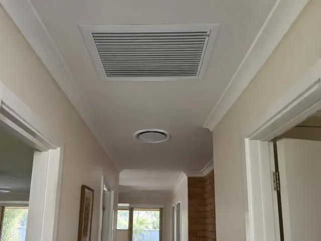 Ceiling return-air grille and round outlet in a beige hallway with white trim in Broadbeach Waters
