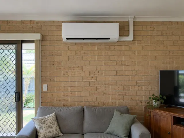Wall-mounted split system above a sofa on a brick feature wall in a living room in Bundall